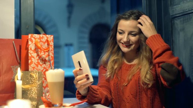Pretty gitl sitting in the cafe at christmas time and doing selfies on smartphone

