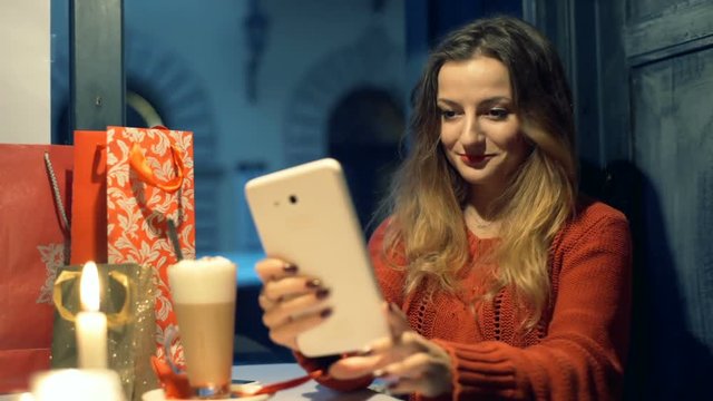 Pretty gitl sitting in the cafe at christmas time and doing selfies on tablet
