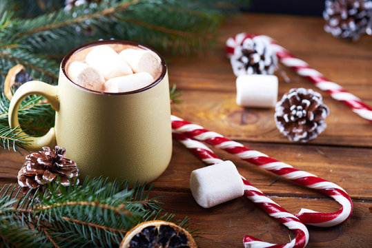 Close view at mug with hot chocolate, christmas tree, tangerines, peppermint stick and marshmallow on a wooden background. Dark photo. Empty space for text