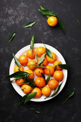 Fototapeta na wymiar Tangerines or mandarins with green leaves on rustic black table from above in flat lay style.
