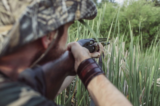 Rear view of hunter aiming rifle on field