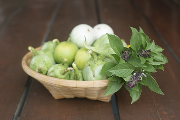 A group of fresh vegetables in a basket. green eggplants, green lemon and sweet basils. Selective Focus