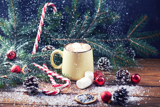 mug with hot chocolate, christmas tree, tangerines, peppermint stick and marshmallow on a snow wooden background with falling snow. Dark photo. Empty space for text. Toned for art effect
