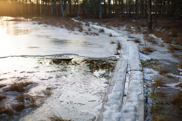Cold winter sunset background of a bog landscape with a wooden boardwalk heading over a lake covered in ice