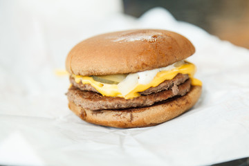 Very tasty and juicy burger made of rye bread, two pieces of meat, pickles, onions, cheese and mushroom sauce. Burger is on white paper