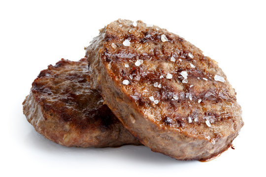 Two grilled hamburger patties with salt isolated on white.