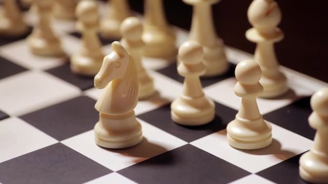 Panning shot of a chess board with a hand moving the white knight.