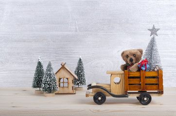 Christmas background with toys-wooden truck carries a teddy bear, Christmas tree, decorations and gifts. Silver and white wood background as a backdrop
