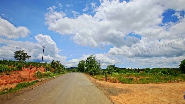 motion along country road to horizon past scooter between plants hilly ground slopes against blue sky with white clouds