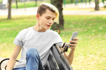 Obraz premium Cute teenager boy sitting with phone in park