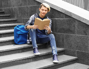 Cute teenage boy with book sitting on stairs outdoors © Africa Studio