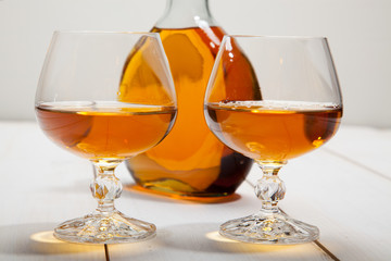 Two glasses of cognac on a white wooden background