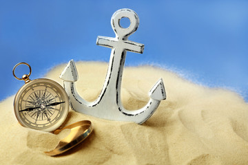 Anchor and compass in sand on blue background. Columbus Day concept