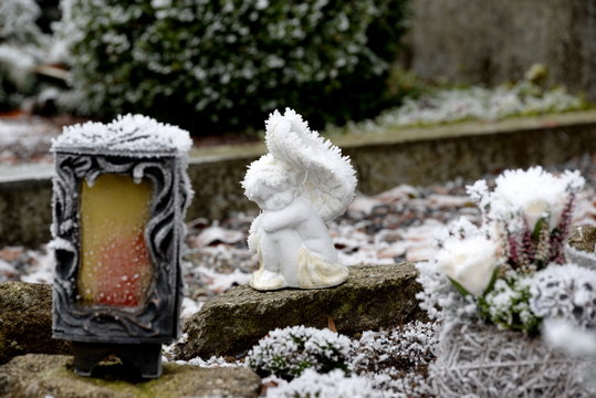 Winterengel, kleiner weißer Engel mit Raureif bedeckt sitzt auf einem Grab