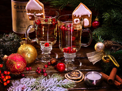 Christmas still life with two latte mug hot drink and wine bottle. Warming mulled wine with cookie in form of house and Christmas ball on Christmas ribbon.