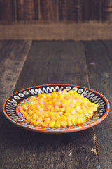 Canned corn in a brown bowl on wooden background. Copy space.