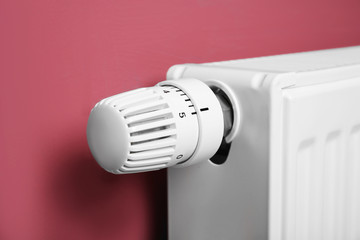 Heating radiator with temperature regulator on pink background, closeup
