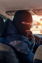 Man in black robbery mask driving a stolen car