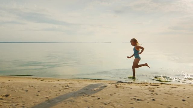 Funny girl runs along the shore, her feet touch the water and flies a lot of splashing