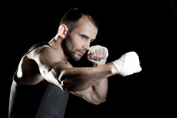 muscular man, tying an elastic bandage on his hand, black background