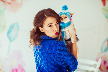 Brunette lady in blue sweater holds chihuahua in winter hat