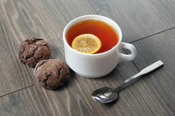 white cup of tea with lemon, teaspoon and cookies on a wooden ta