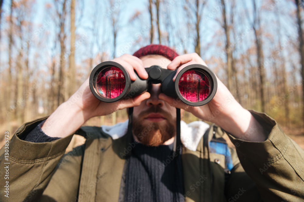 Poster Handsome bearded man looking at field-glass in the forest.