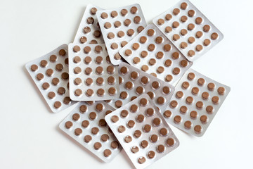 Many brown pills lies in  containers on a white background.