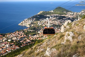 Obraz premium ドブロヴニクの山の斜面を昇って行く赤いケーブルカー アドリア海の海の色とドブロブニク旧市街の家々の赤茶色の屋根が素晴らしいコントラストを創り出していた。