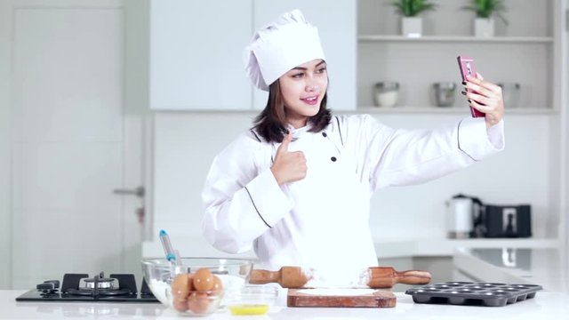 Beautiful female chef making cake in the kitchen and taking selfie picture with a mobile phone