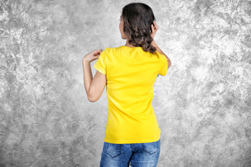 Obraz na płótnie Canvas Young woman in blank yellow t-shirt standing against grey textured wall