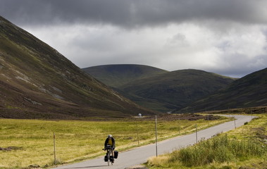 Cyclist on road through the Glen Clunie hills and Grampian Mountains, Scotland