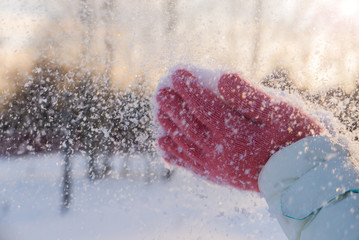 Young woman holding snow on palms and blowing it