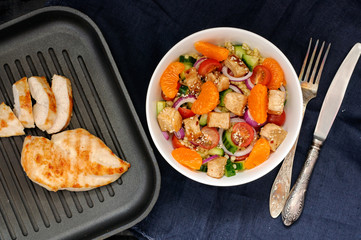 Healthy salad bowl with cuscus, tomatoes, cucumber, chicken, tangerine and sesame seeds