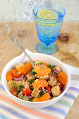 Healthy salad bowl with cuscus, tomatoes, cucumber, chicken, tangerine and sesame seeds