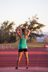 Female fitness athelete getting ready to run a sprint race on a tartan athletics track.