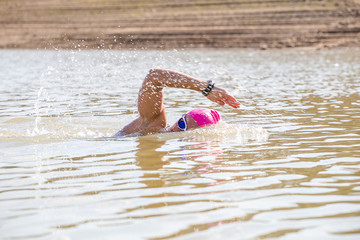 Female triathlete swimming in a dam while competing in a triathlon