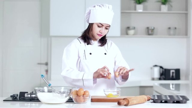 
Pretty young woman making cake in the kitchen and break an egg on a bowl
