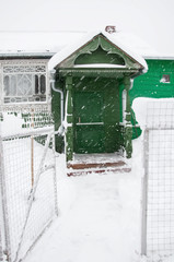 Snowy front steps of country house in Russian village in winter. Green rural house with carved window frame