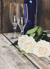 White roses, sparkling wine bottle, champagne glasses on a woode