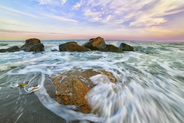 Beach at sunset (sunrise) beautiful sky with clouds. waves run ashore, taken on a long exposure, the ripples on the water and foam left a drawing in the sand. waves and mist shrouded misty water. 
