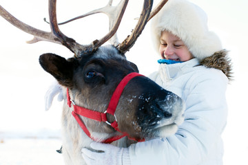 Happy little girl hugging her reindeer. Winter playtime.