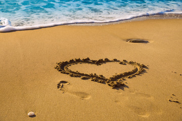 Drawing a heart on the beach sand on the beach with sea waves in the background. Selective focus. Beautiful deserted beach. Trace of human foot on the sand.