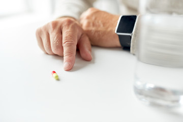 close up of old man hand with pill and smart watch