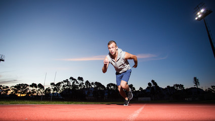 Obraz na płótnie Canvas Male sprinter athlete on a tartan athletic track getting ready f