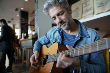Mature trendy guy playing the guitar in a bar