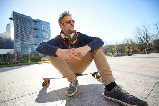 Trendy urban guy sitting on skateboard in park