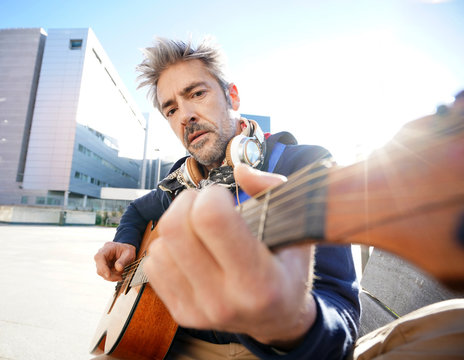 Mature trendy guy playing the guitar in the street