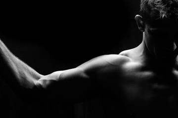 Naklejka na ściany i meble Male fitness model showing muscles in studio with a black backgr