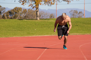 Fototapeta premium Male Athlete sprinting on a tartan athletics track on a bright s